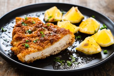 Baked marinated turkey cutlet and lemon wedges on black plate