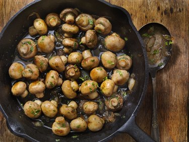 an overhead photo of a butter and garlic mushrooms with onions cooked in a cast iron skillet on a wooden table