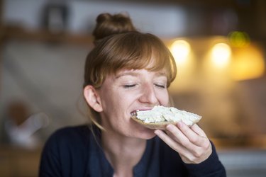 Young woman eating bread with cream cheese because she's craving carbs