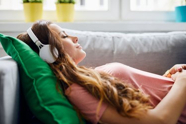Portrait of a beautiful young woman lying on sofa with headphones on and closed eyes, relaxing