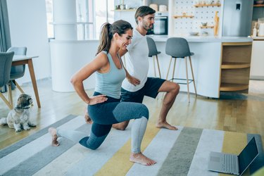 caucasian man and woman doing lunges at home in front of a computer