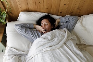 Person with eyes closed yawning in bed at home