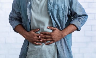 an unrecognizable person in a blue shirt touching their abdomen because they have stomach pain when standing up