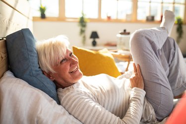 Happy senior woman with gray hair lying in bed, as an example of sleep for healthy aging