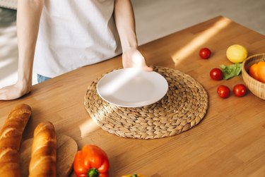 Woman hold empty white plate on the wooden table in the kitchen.