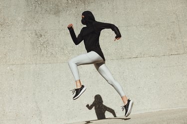 side view of a woman in a hijab sprinting in front of a concrete wall
