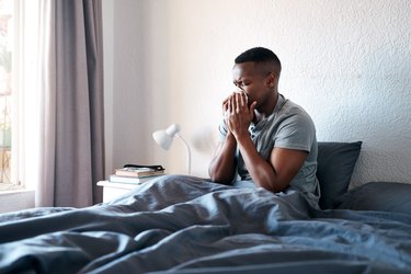 man blowing his nose in bed after waking up congested