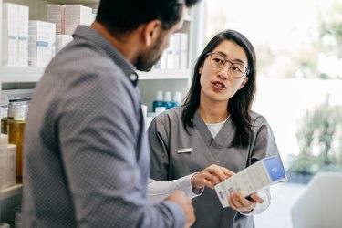 a pharmacist with long black hair wearing glasses and wearing grey scrubs and talking to a customer about common mistakes with prescription drugs