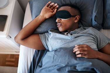 一个人睡在床上,一个黑色的睡眠面具在他们的眼睛