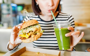 年轻女子喝绿沙拉 并吃汉堡 素食快餐