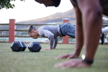 closeup of dumbbells and two men doing push-ups outside, gaining the health benefits of strength training