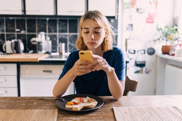 Young woman using smartphone at breakfast to calculate food's nutrient density