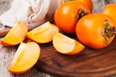 persimmon fruits, whole and sliced, on wooden board