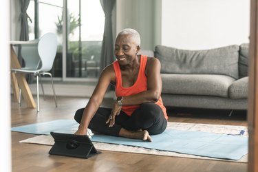 A black senior woman taking an online yoga class in her living room