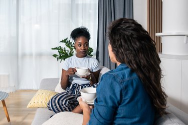 Two young people sitting on a sofa drinking tea and talking