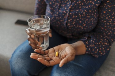 Black person holding a zinc supplement pill in had with a glass of water