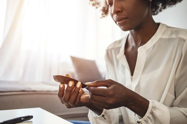 Woman with glucometer checking blood sugar level at home.