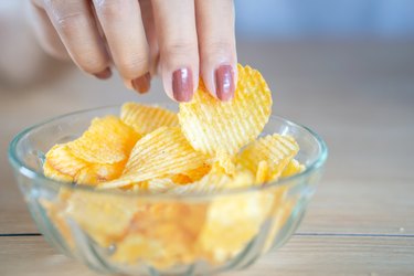 closeup woman hand eating potato chip in bowl