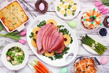Traditional Easter ham dinner. Top view table scene on a white wood background.