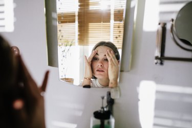 a person looks in the mirror and holds their face in a white bathroom
