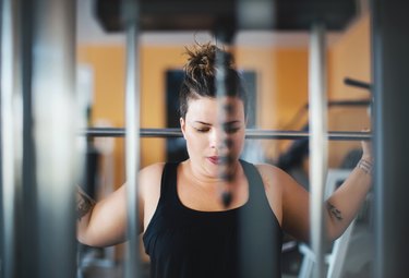 view through an exercise machine of a person with a brown ponytail lifting weights, as an example of things that cause high blood sugar without eating