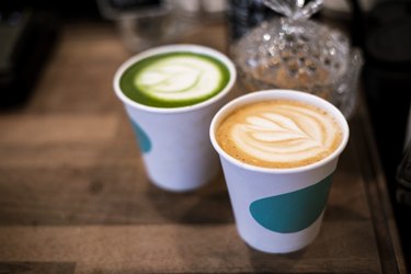 overhead shot of latte and green tea in white to-go cups on wooden counter