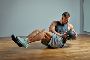 Strong man doing Russian twist exercise with a medicine ball. Photo of man perfect physique on grey background. Strength and motivation