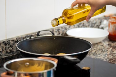 woman pouring cooking oil from bottle into frying pan