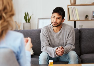 a young adult sitting on a gray couch attending a therapy session with a psychiatrist