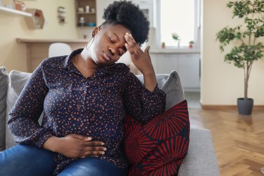 a woman sitting on the couch at home with her hand over her belly because of indigestion after eating