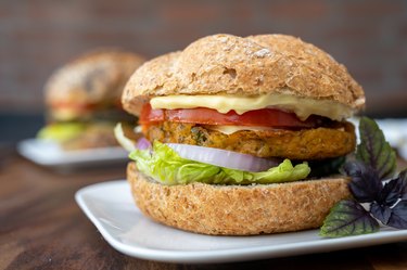 A veggie burger sandwiched between cheese, tomato, onion, lettuce and bread on a plate