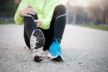 Runner with a muscle cramp after workout in the city park in cold weather