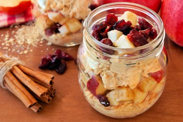 Slow cooker oatmeal recipe for breakast with apples and cranberries on a wooden table next to fresh cinnamon.