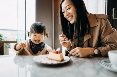 父母与棕色长发和一个年轻的孩子,马尾辫坐在一张桌子分享一块蛋糕