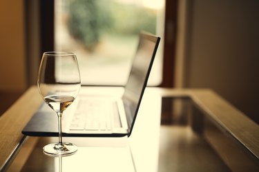close up of a wine glass next to a laptop on a glass table