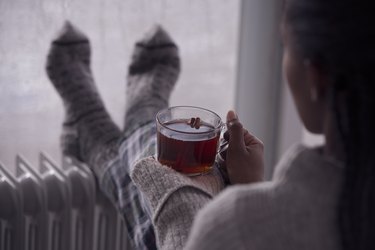 Over the shoulder image of a woman drinking tea at home in cold and wet weather.