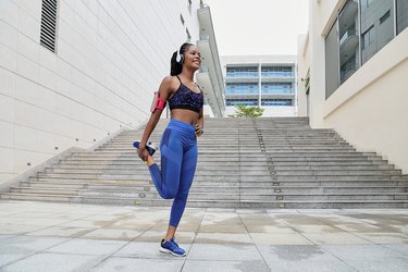 Woman doing a standing quad stretch after her workout near the stairs outdoors