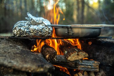 Campfire baked potato cooking over firy coals in the wilderness,