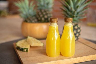 Two bottles of of acidic pineapple juice on a wooden cutting board