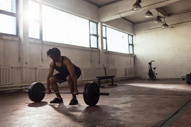 man performing a barbell deadlift exercise in an empty loft with windows