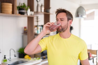 Man in yellow shirt drinking SlimFast shake in kitchen to show celebrity slim thick quick shakes side effects and why SlimFast cans are so thick