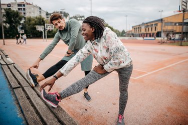 two people doing a leg stretch on a bench outside pre-workout