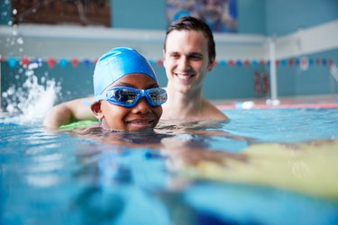 swimming Coach Giving young child Holding Float One To One Lesson In Pool