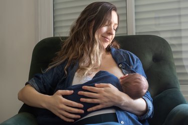a parent sits in an armchair breastfeeding a newborn