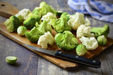 Brussels sprout, broccoli and cauliflower chopped on a wooden cutting board resting on a wooden table.