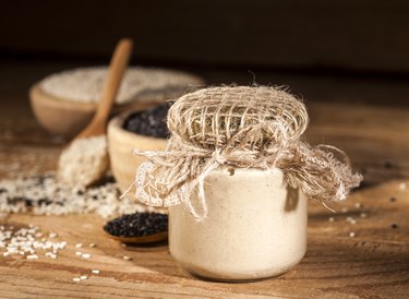 Fresh calcium-rich sesame tahini in a glass jar and seeds in wooden bowls and spoons