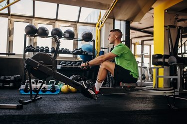 Person wearing a green T-shirt and black shorts using a rowing machine at the gym