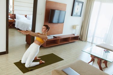 Fit person wearing white leggings and with hair in a bun does the leaning camel at home on a mat