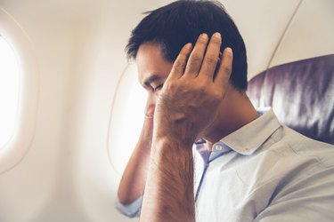 a person wearing a button down shirt sitting on a plane holding their ears
