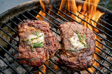 Two Delicious Thick Juicy Ribeye Steaks On A Flaming Grill
